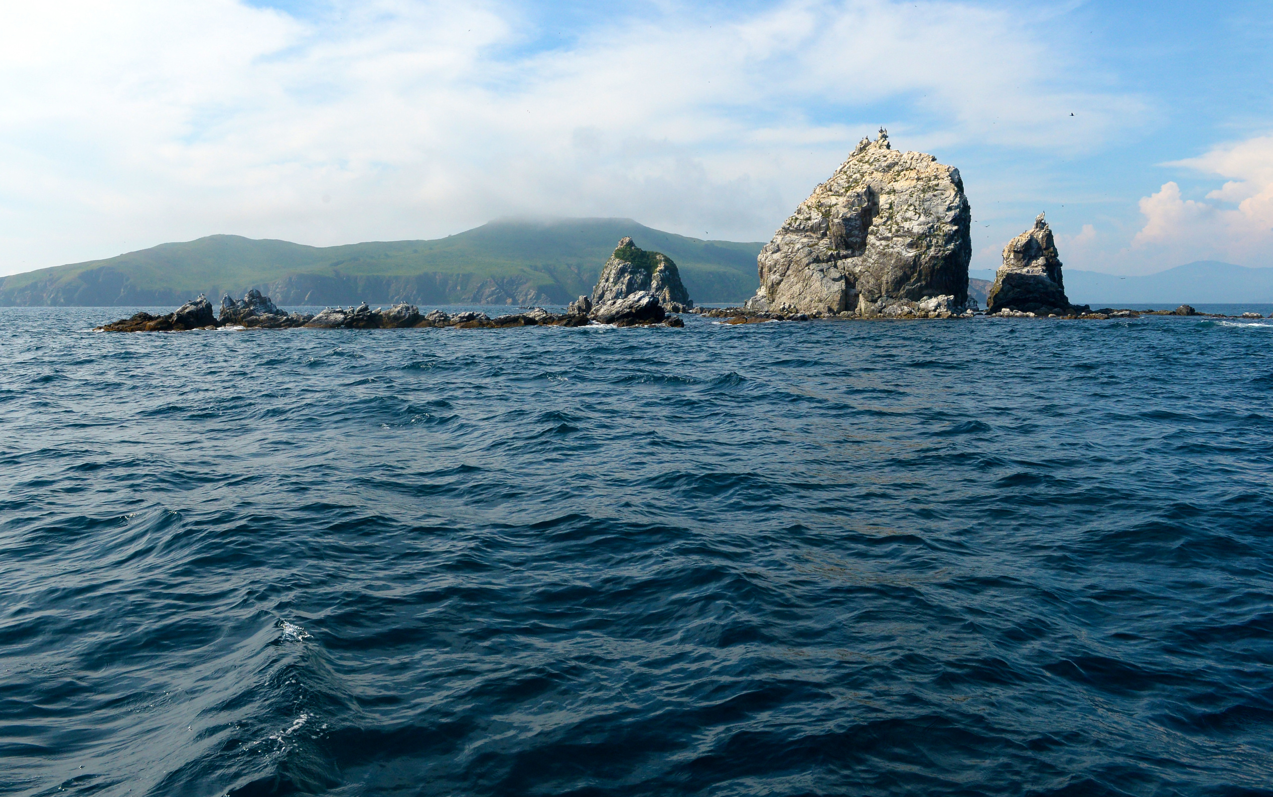 Скалы на фоне острова Аскольд, вершины которого часто укрывают туманные облака. Фото: Юлия Гопиус