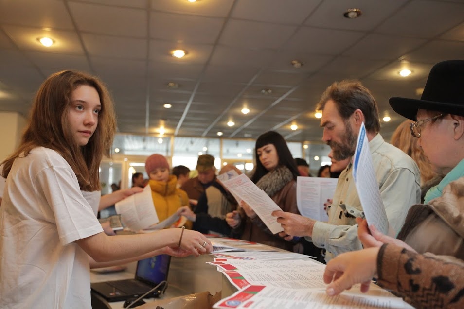 Волонтеры у стойки регистрации раздают программы