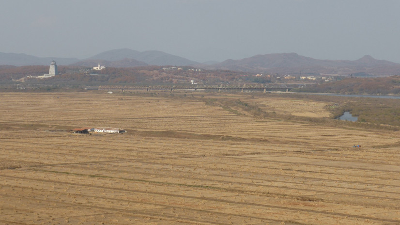 The Friendship Bridge, which connected the DPRK with the USSR in 1959. The fields of the DPRK in the floodplain of the Tumen River in the foreground; the Russian village of Khasan on the left (in the background) bank of the river. The white tower on the left is on Chinese territory. Photo: wikipedia.org